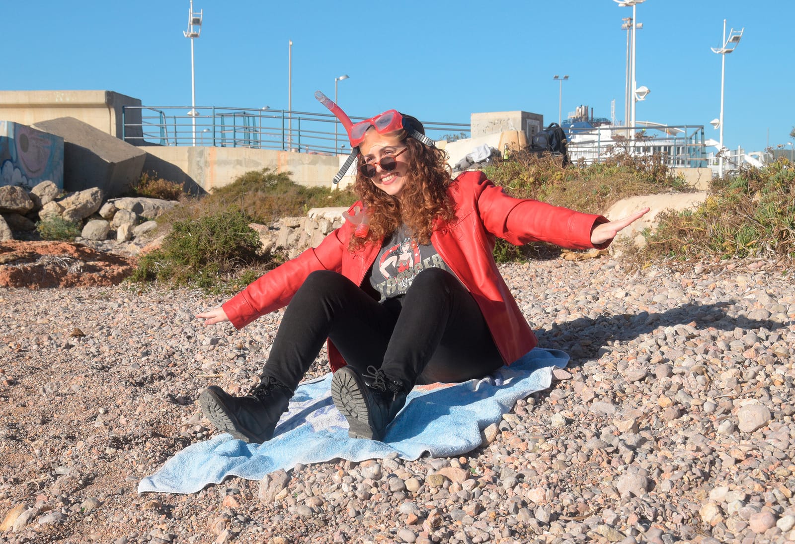 Irene con chaqueta roja y pantalones negros sentada en una playa